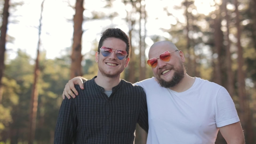 Gay Couple in heart sunglasses stay at park and show in camera red heart simbol