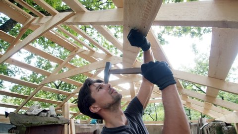 handsome man hammers a nail into the roof board of his garage