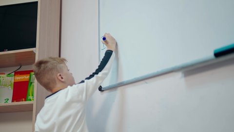 KYIV, UKRAINE - May 2020: Boy studying at school. Schoolboy writing on a whiteboard with a marker in the classroom. Elementary education.