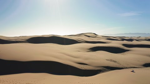 Aerial slow motion video of the wild desert nature. Drone flying over the beautiful golden sand dunes in the shape of waves on sunny day with blue sky above. 4K California scenic nature landscape, USA