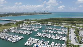 Bird-eye view on the island with yachts at marina harbor. Beautiful slow motion drone video for yacht business. Marine club with Miami downtown on background. 4K aerial water sport and transportation