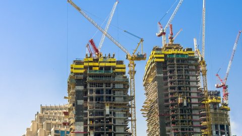 Construction site in Dubai downtown, United Arab Emirates, with many working cranes on two tall buildings and blue sky, time lapse footage