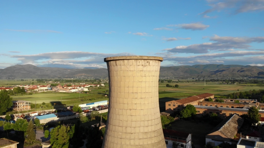 Coal plant station with tall tower and buildings on a rural landscape with green fields on cloudy sky background