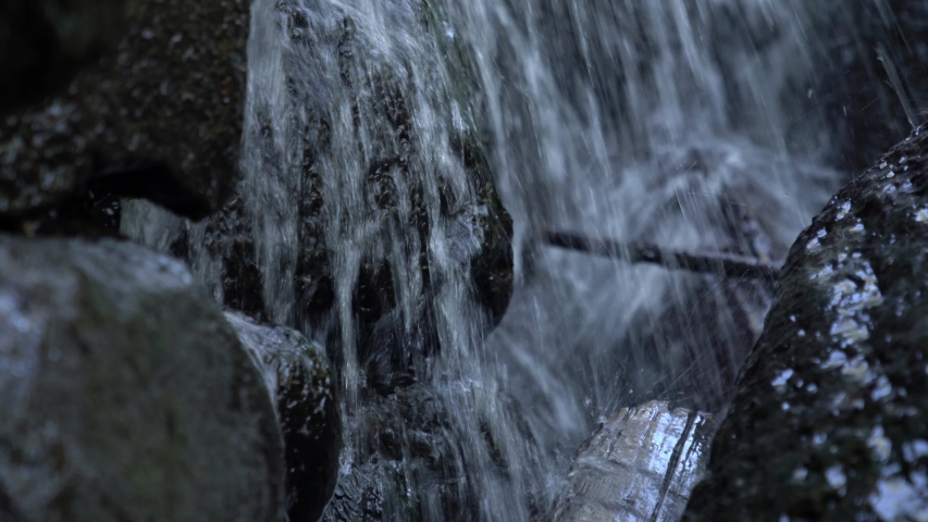 Close up of white water flowing over the rocky surface of a man made waterfall cascade with a view between boulder rocks covered in dark slippery algae and wet.