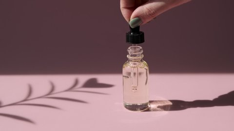 Beauty moisturizing essence in oil dropper glass bottle. Hydrating serum, vitamin for face skin. Oily drop falls from cosmetic pipette on pink background. Bottle mock-up. 
