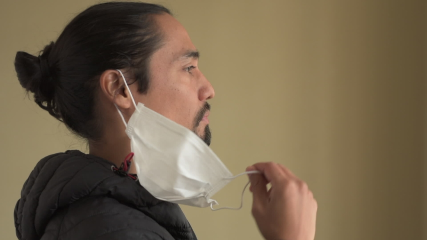 Profile portrait of a handsome latin man with a beard and tied hair takes off his mask breathes deeply and smiles ending his quarantine and the covid-19. Quarantine concept. | Shutterstock HD Video #1055689748