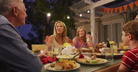 Multi-generation Caucasian family spending time in garden together, sitting at a dinner table, eating and talking, in slow motion.