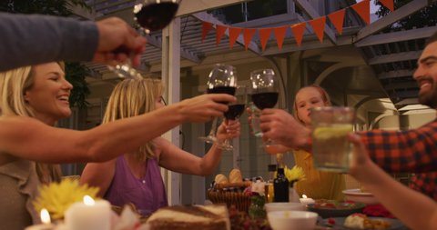 Multi-generation Caucasian family spending time in garden together, sitting at a dinner table, making a toast, in slow motion.