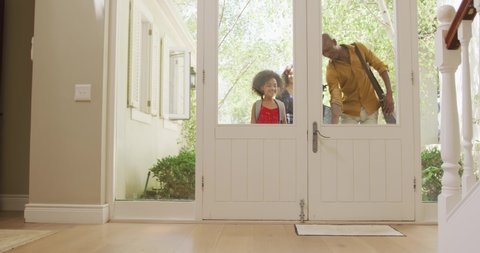 African American couple, their son and daughter entering the front door of their house, the children wearing backpack and running ahead, in slow motion.
