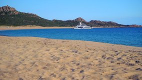 Amazing view of the sandy beach on a sunny day with azure clear water. Motor boat and yacht. People are sunbathing. Luxury holidays on the islands. Tropical beach with sun loungers and parasols