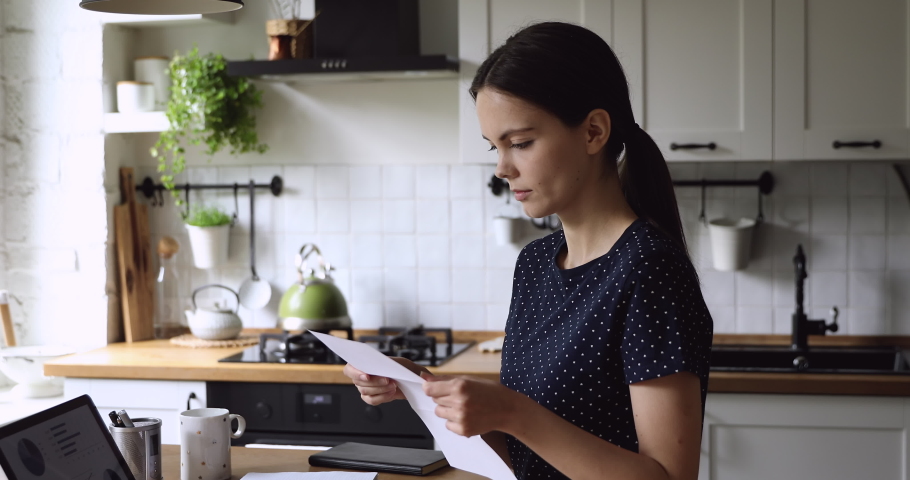 Woman standing in home kitchen hold written paper read letter frowns feels frustrated due horrible news. Loan late payment, unexpected bank debt, high taxes, bad exam result, negative feedback concept Royalty-Free Stock Footage #1055702624