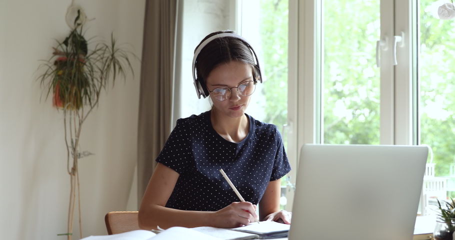 University student in headphones eyeglasses studying by videochat videocall use laptop noting information talk with s schoolmate work on common task distantly. On-line tutoring, self-education concept Royalty-Free Stock Footage #1055702726
