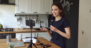Woman in home kitchen put phone on tripod record video describe how use make up brush, facial cream, tell about beauty treatment benefit, cosmetic product ad. Influencer marketing goods review concept