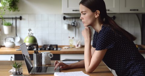 Young woman leaning on kitchen table use laptop looks into distance feels worried consider over problem solution, student thinking about ideas topics for essay, freelance work activity at home concept