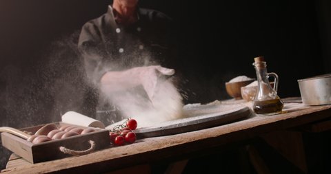 Epic dynamic shot of senior professional chef throwing flour onto table, making flour clouds before making pizza isolated on black background close up 4k footage