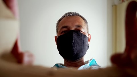 A man in a protective black mask opens a paper delivery bag from an online store. Coronavirus pandemic quarantine, portrait of a man, home isolation. View from the packaging on the man. : vidéo de stock