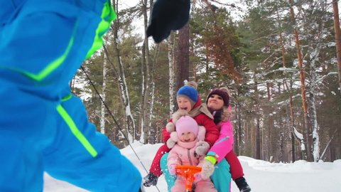 joyful family rides on orange sled and father runs pulling halter in dense forest with large trees extra slow motion closeup