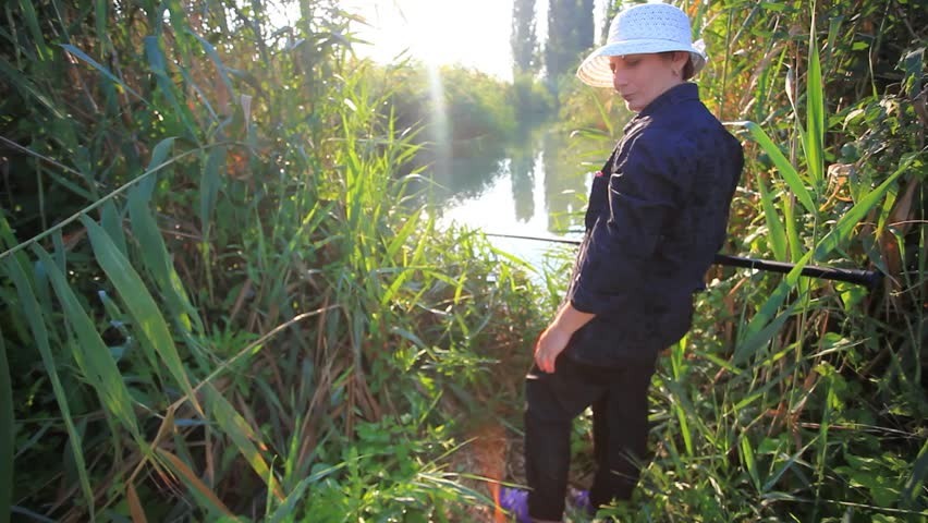  woman aged in hat fishing at pond in the morning