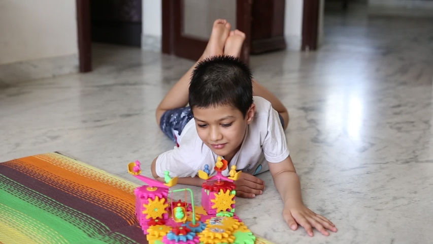 A six year old Indian child, playing with a his self created toy from blocks depicting a fair or fate with merry go rounds , powered by battery 