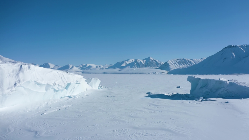 Droneflight in the middle of the polar arctic region close to the north pole showing a white, icy and frozen fiord with huge glacier ice bergs and snowy mountain peaks, ellesmere island Royalty-Free Stock Footage #1055714297
