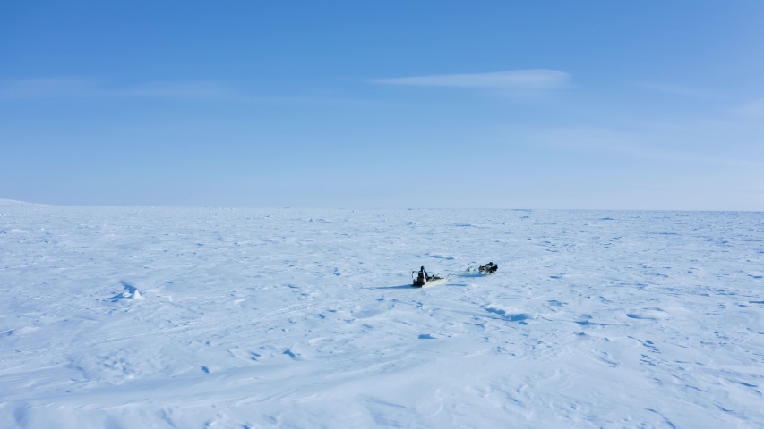 A traditional Inuit or Eskimo is going hunting with his husky dogs and sled driving over endless white and ice towards horizon in the extreme, cold and icy arctic region, north pole Royalty-Free Stock Footage #1055714984