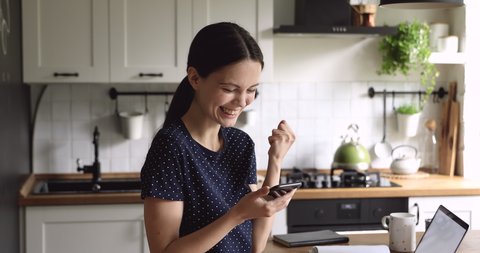 Woman spend time on kitchen hold phone receives long-awaited sms great news makes Yes gesture feels incredible happy, scream with joy laughing enjoy moment of personal achievement goal succeed concept