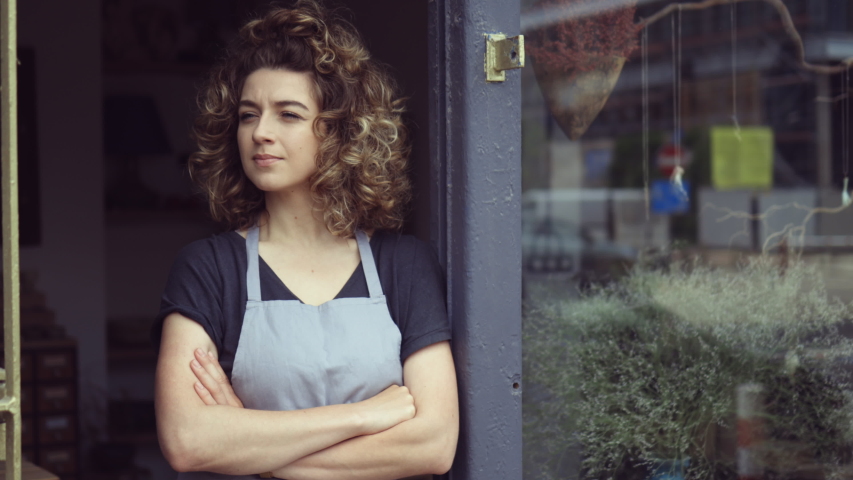 Smiling young woman at the door of her shop welcoming customers