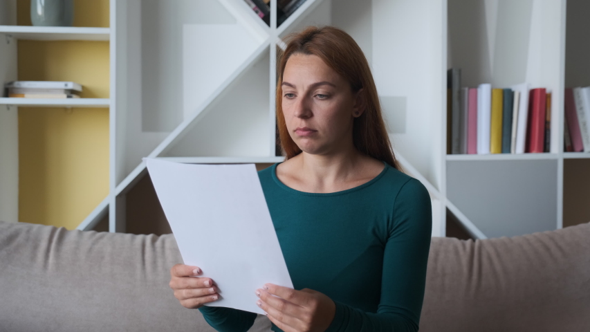 Sad woman sitting on couch at home reads received bad news holds documents paper letter feels desperate about financial problems, girl student worried college expulsion concept. Royalty-Free Stock Footage #1055717468