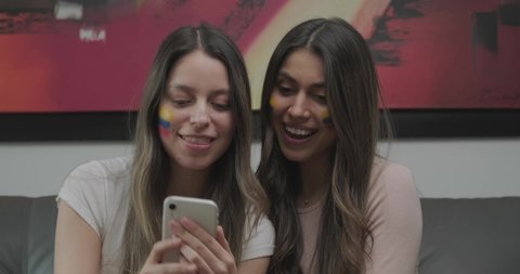 Two Lovely Colombian Women Sitting On A Sofa Smiling While Taking Photos Using A Smartphone - Slow Motion
