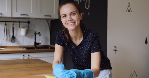 Young housewife do chores wear rubber protective gloves use rag cleans wooden surface of kitchen table enjoy process. House cleaning services worker work with effective home cleaning products concept