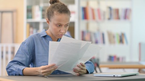 Young African Woman Reading Documents in Library