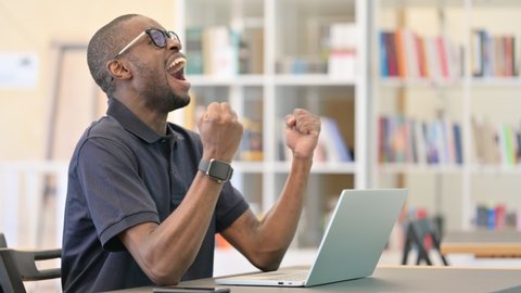 African Man Celebrating Success on Laptop in Library