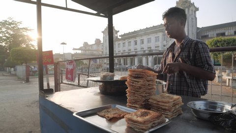 Yangon / Myanmar - 02 23 2019: Asian street vendor selling fresh paratha pancakes during sunrise in Yangon,Myanmar