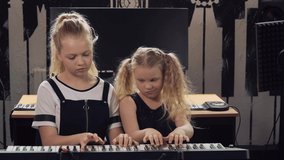 Two girls play the synthesizer. Sister teaches to play a musical instrument.
