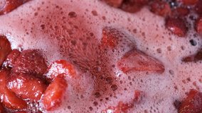The process of making strawberry jam in its own juice with the addition of sugar in an open bowl on a gas stove macro video shooting