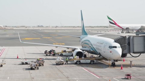 Muscat, Oman - May 6, 2019: Loading luggage in a plane. Male workers are load passenger luggage into the cargo hold of the aircraft of Oman Air airline. Suitcases move along the conveyor loading belt
