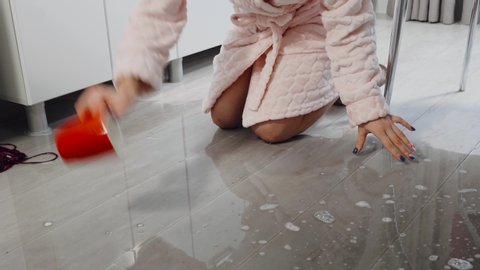 A woman at home wipes water with a mug from the floor.
