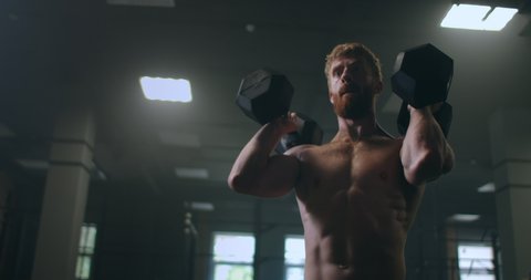 male athlete lifting heavy dumbbells over his head performing exercises in the gym. achieving the difficult goal of taking care of the body and health.