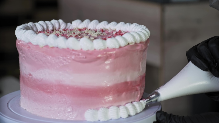 pastry chef decorates with help of pastry bag edges of sweet cake with protein cream, concept of baking