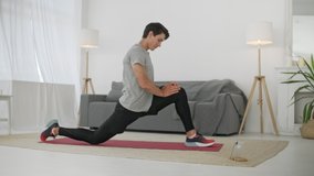Handsome Young Man in a Gray T-Shirt and Black Shorts Does Sports at Home Online.Doing Sports and Fitness Training at Home. Healthy Lifestyle. Stretching, Leaning Forward