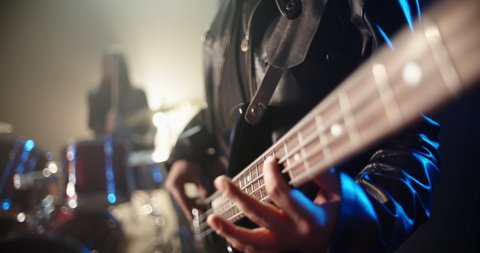 Closeup shot of cool rock bass player making a solo with band mate drummer on background - rock music concept 4k footage