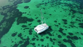 Aerial drone video of catamaran sailing yacht anchored in tropical exotic emerald sea coral reef bay