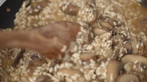 Close-up of mixing with a wooden spoon mushroom risotto. Concept of preparing mushroom risotto with vegetable stock in a pan in 4k
