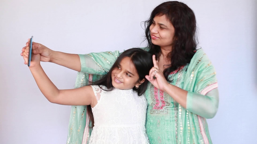 Indian little girl with her mother using tablet computer at home to take selfie 