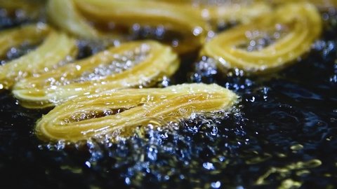 Close up of delicious looking golden churros being fried in boiling oil in slow motion. Tasty food and cooking concept.
