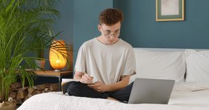 Young male student study online with tutor teacher, conference, video call chat learn language and makes notes sit at home in badroom and look at laptop computer.
