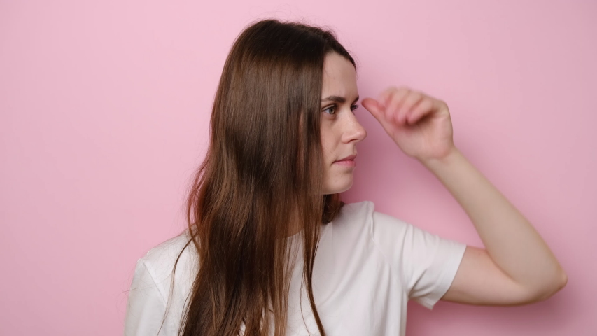 Attentive brunette woman isolated on pink studio background carefully looking far away inspecting horizon, holding hand over eyes peering distance, pointing happily to camera when discovered you Royalty-Free Stock Footage #1055771012
