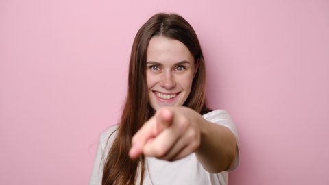Attentive brunette woman isolated on pink studio background carefully looking far away inspecting horizon, holding hand over eyes peering distance, pointing happily to camera when discovered you