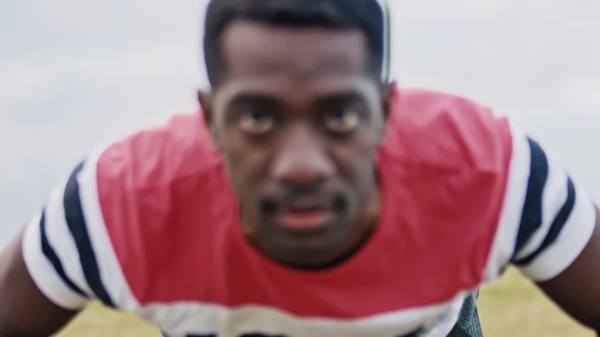 Slow-motion close up of a black athlete doing push-ups while staring intensely at the camera.