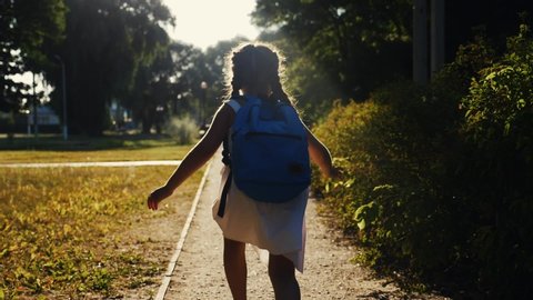 schoolgirl kid with a backpack run through the park home from school dream on a sunny day. daughter little girl with school backpack running home after school. concept education run children learning